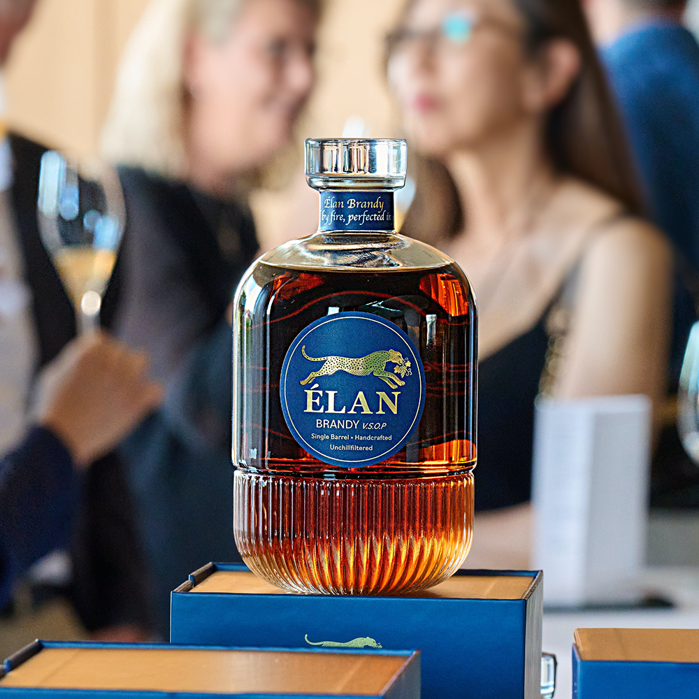 Eine Flasche Elan Brandy mit einem blauen Etikett, auf dem ein goldener Gepard abgebildet ist, auf einer blauen Geschenkbox.